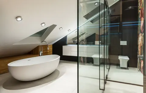 Creative design of bathroom with bath against shower cabin with glass wall on tiled floor in attic