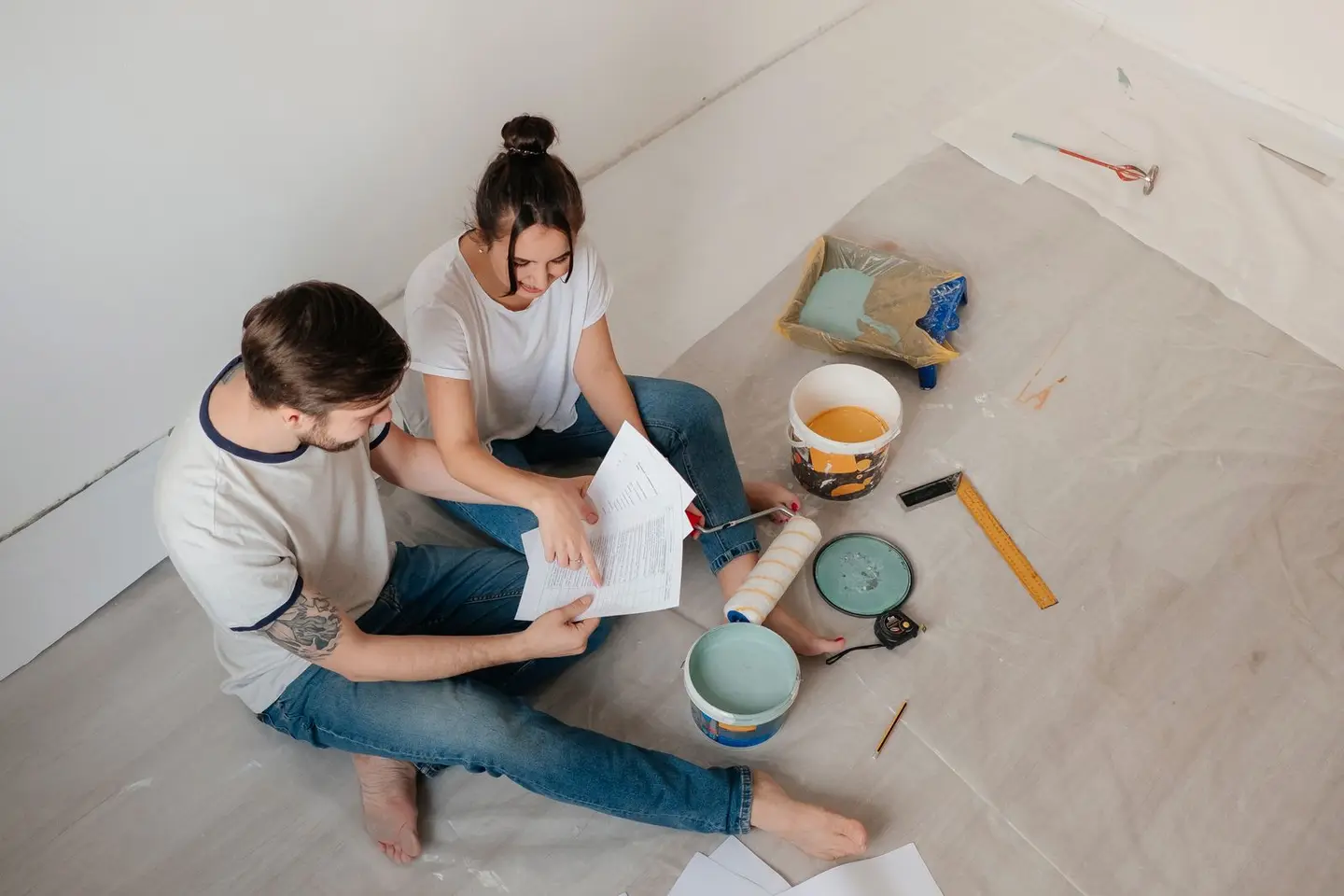 A couple sitting on the floor, reviewing documents amidst home renovation materials.