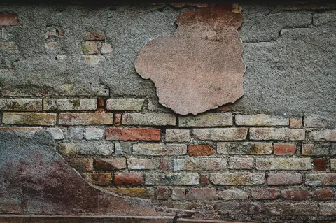 Close-up of a weathered brick wall with peeling plaster revealing rustic textures.