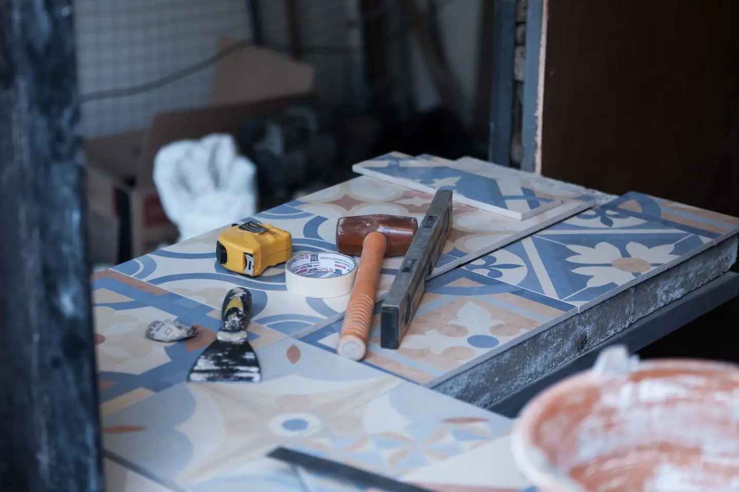 Tools and tiles on a construction site, ready for tiling work. Includes trowel, tape measure, and adhesive tape.