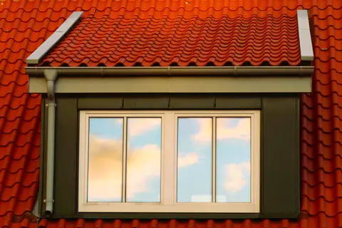 A close-up of a rooftop window reflecting the sky on a red tiled roof.