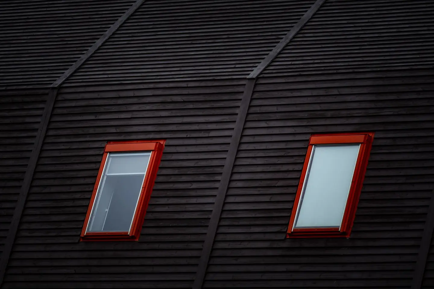 Close-up of a dark wooden roof featuring two red-framed windows adding a modern flair.