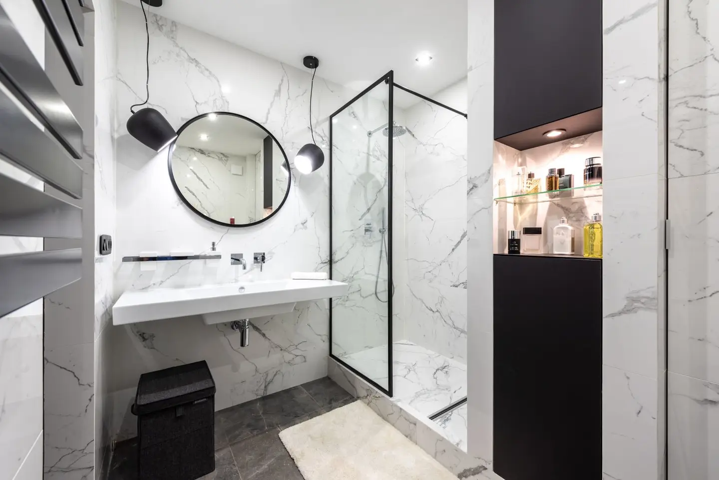 Shower room against washbasin and mirror between shiny lights in bathroom with assorted perfume in bottles on shelves