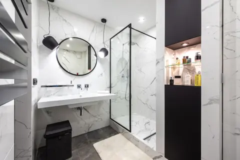 Shower room against washbasin and mirror between shiny lights in bathroom with assorted perfume in bottles on shelves